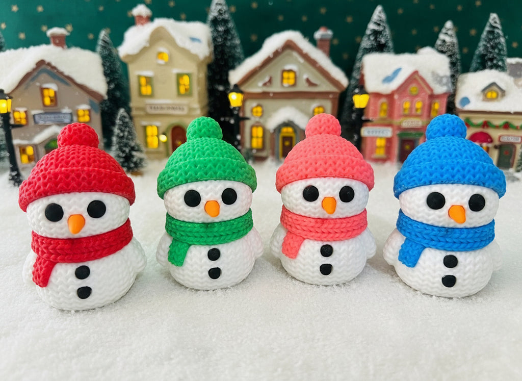 Four crocheted snowmen with colorful hats and scarves on a green fabric background.